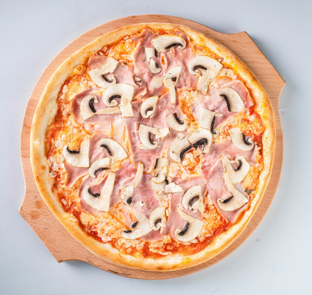 Pizza au jambon et aux champignons sur une planche en bois